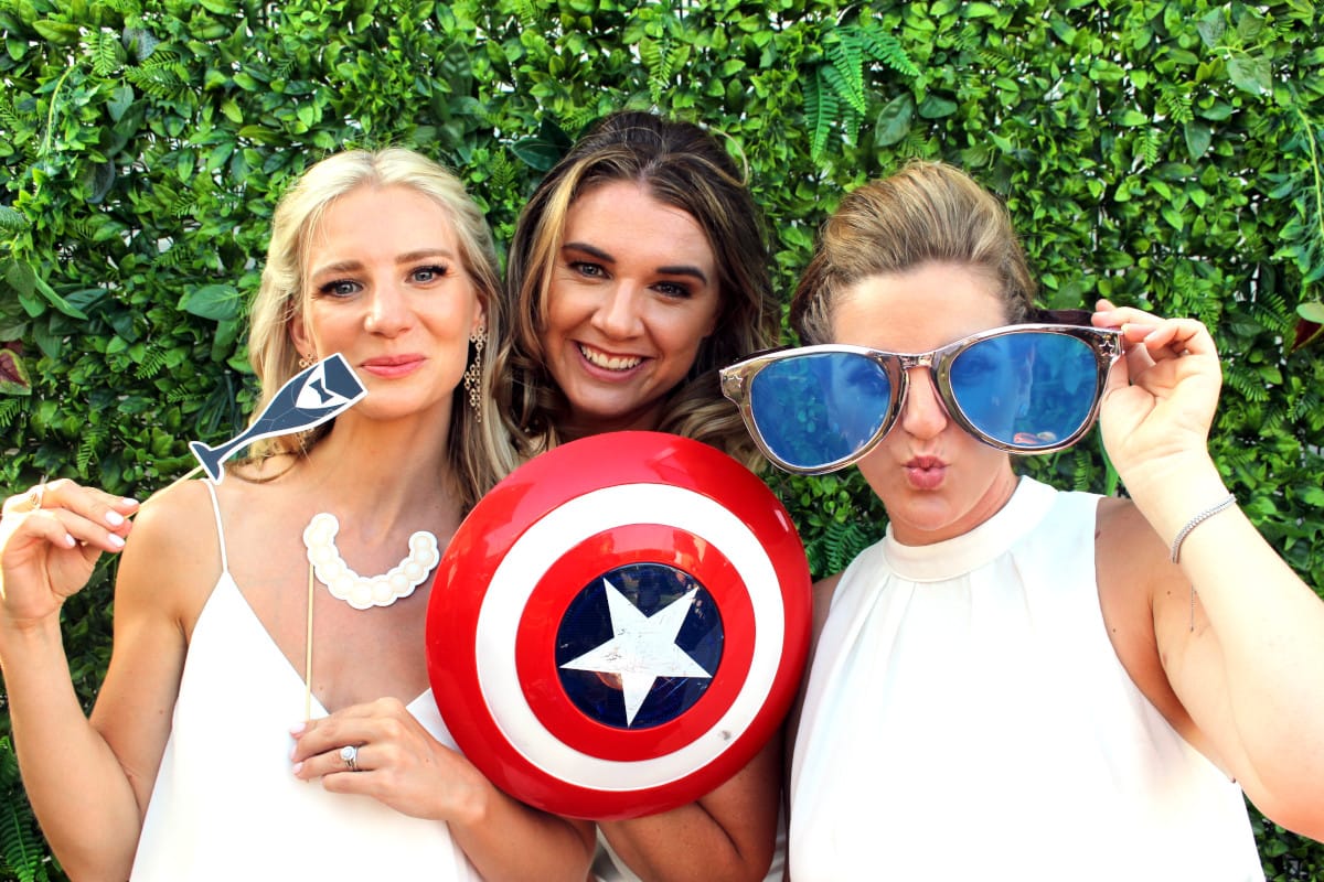 Three girls posing for photo booth with props shield, glasses and drink