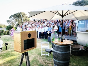 Photo booth set up in front of crowd at an outdoor wedding