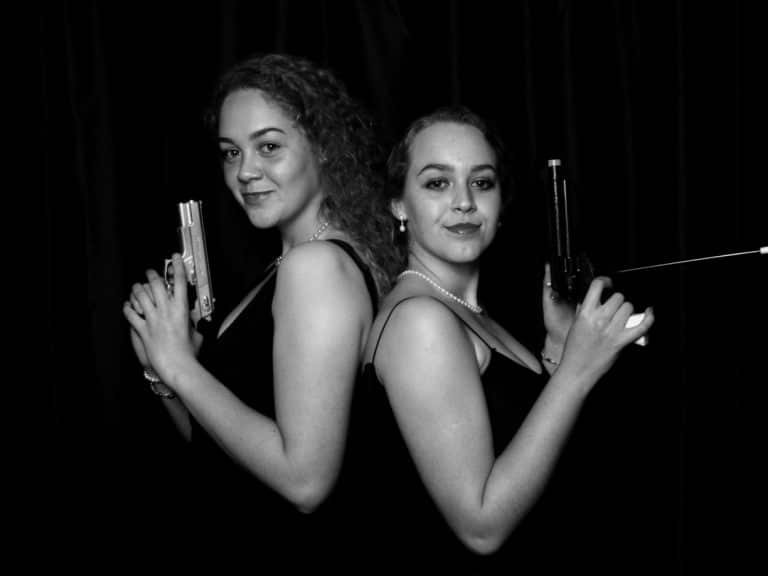 Two girls back to back with gun props posing for photo booth shot