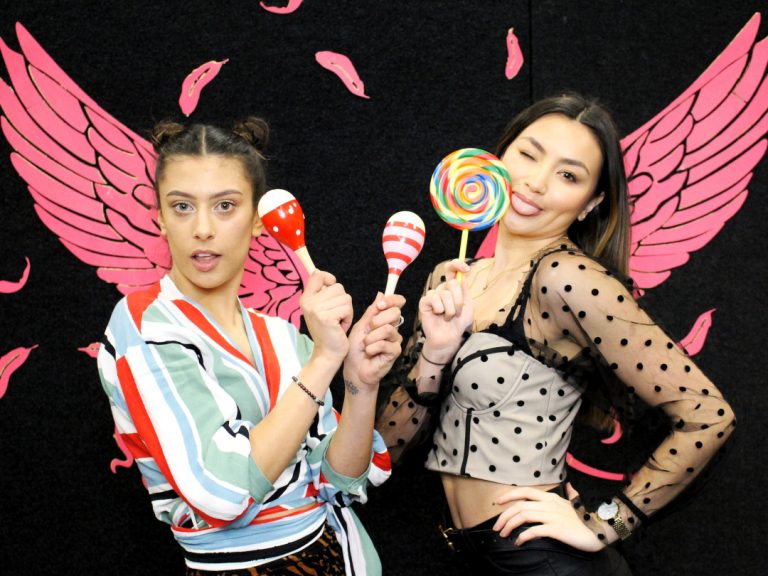 Two girls posing in front of pink feather wings with lollipop prop